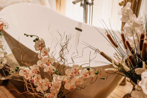 Detail shot of a white vintage clawfoot bathtub at MI Studio Space, decorated with overflowing white orchids, dried pampas grass, and floral stems.