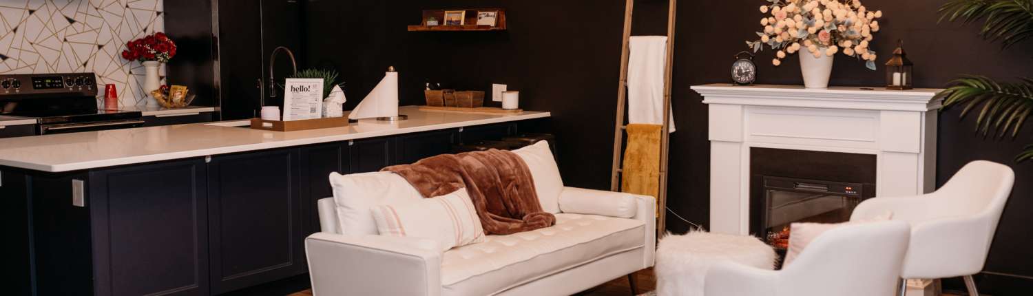 Spacious lifestyle photography studio featuring a modern kitchen with navy cabinets, a white fireplace mantel with floral decor, and a cozy seating area with a white sofa and patterned rug.