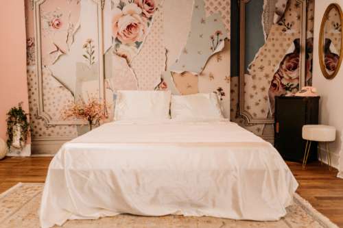 Romantic boudoir photography set featuring a white bed with cream linens, vintage floral wallpaper murals, a pink rotary phone, and a white velvet stool at MI Studio Space.