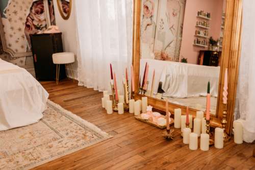 Grand ornate gold floor mirror at MI Studio Space surrounded by an arrangement of white pillar candles and colorful tapered candles on rustic wood floors in the boudoir suite.